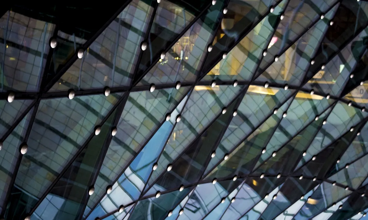 Reflections sliding across a glass facade of diamond-shaped panes and metal nodes